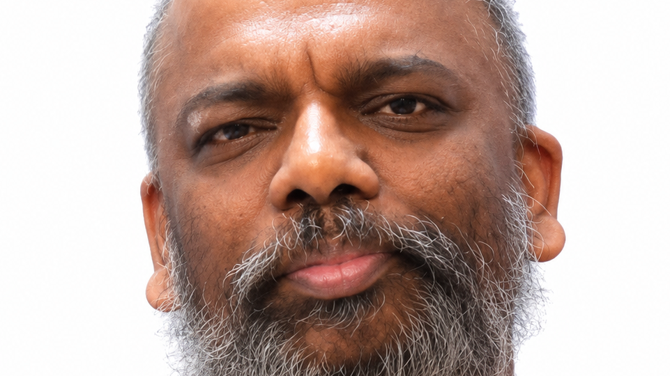 Close-up portrait of a man with a grey beard looking at the camera against a white background.