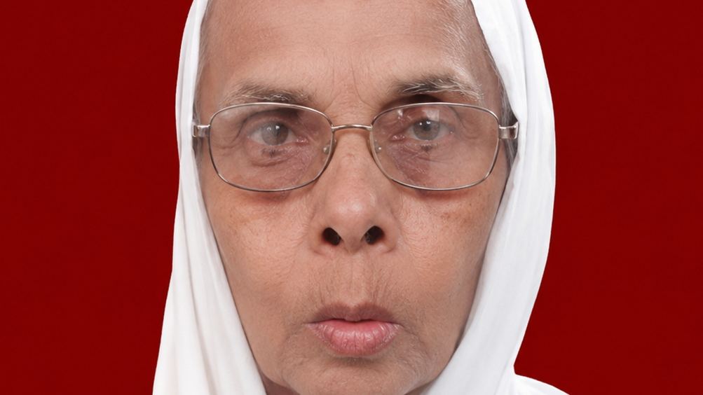 Close-up of a woman wearing a white headscarf and glasses, with a solid red background.