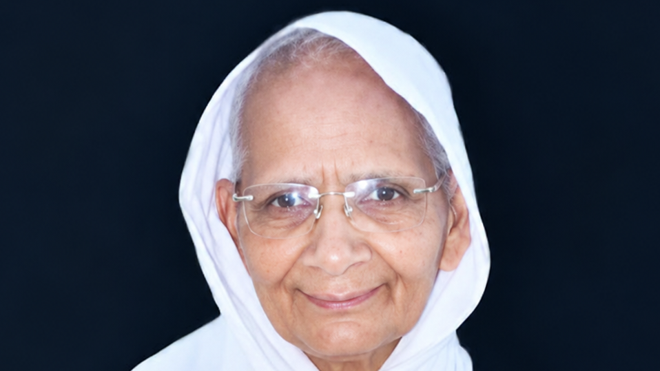 Portrait of an elderly woman wearing a white headscarf and glasses, smiling at the camera.