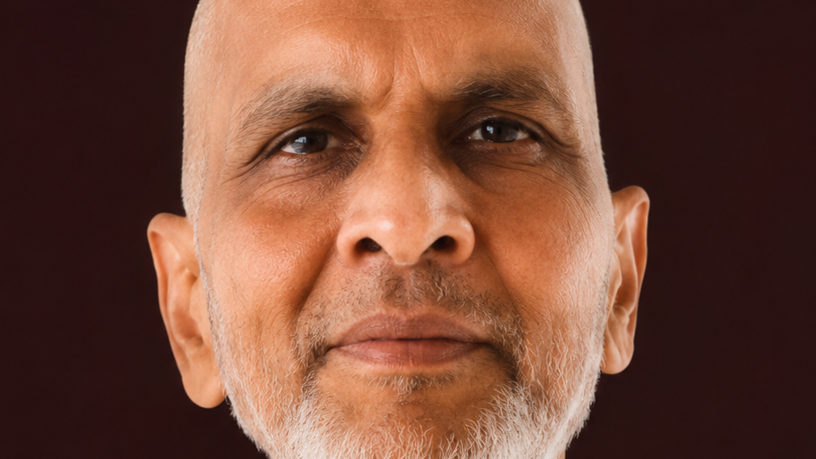 Close-up portrait of an older man with a gray beard, calm expression, against a dark background.