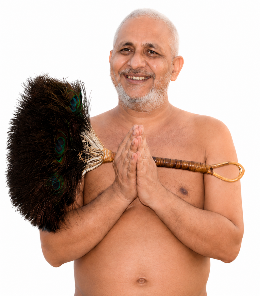 Smiling, shirtless man with gray beard holds a large feather fly whisk on his shoulder, hands together in a prayer pose.