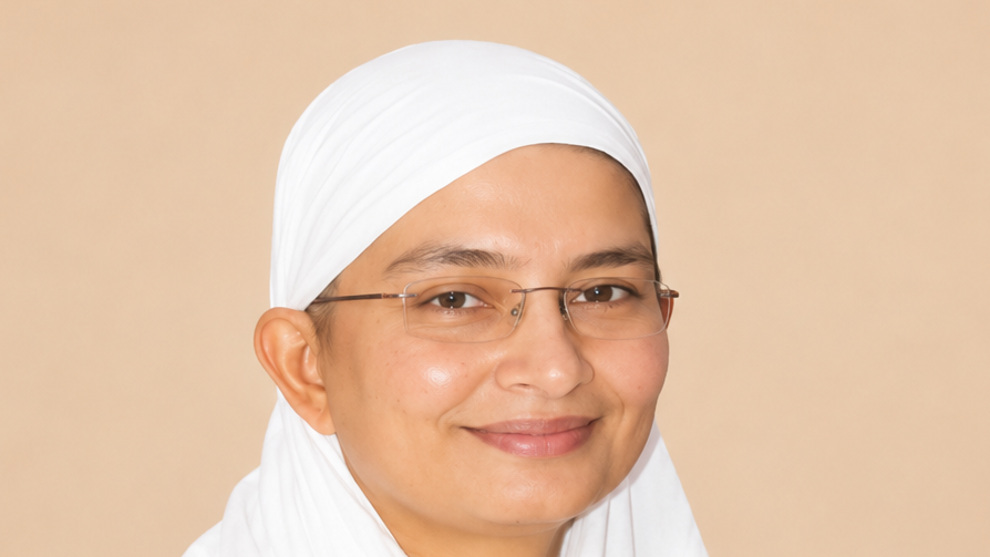 Smiling woman wearing a white hijab and glasses against a beige background.
