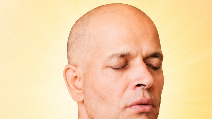 Close-up of a bald man with eyes closed, meditating against a radiant yellow glow background.