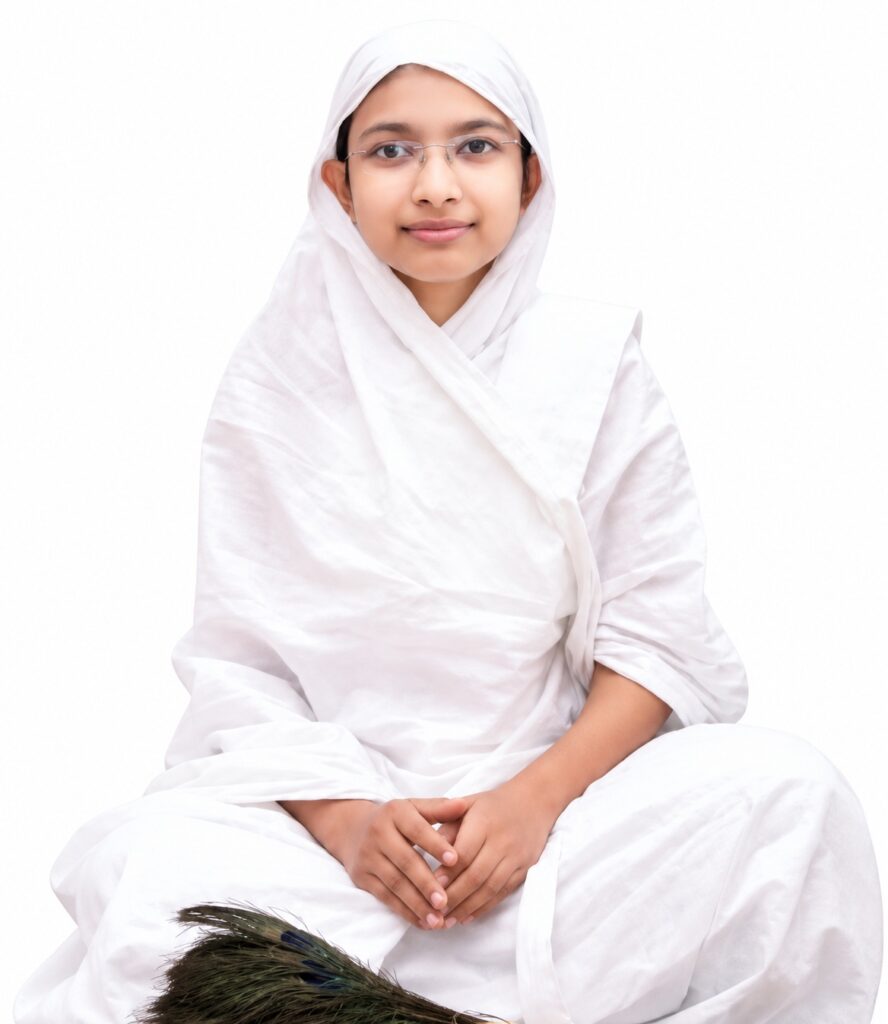 Young girl in a white hijab and robe sits cross-legged with hands folded, wearing glasses, against a plain white background; a peacock feather appears in the foreground.