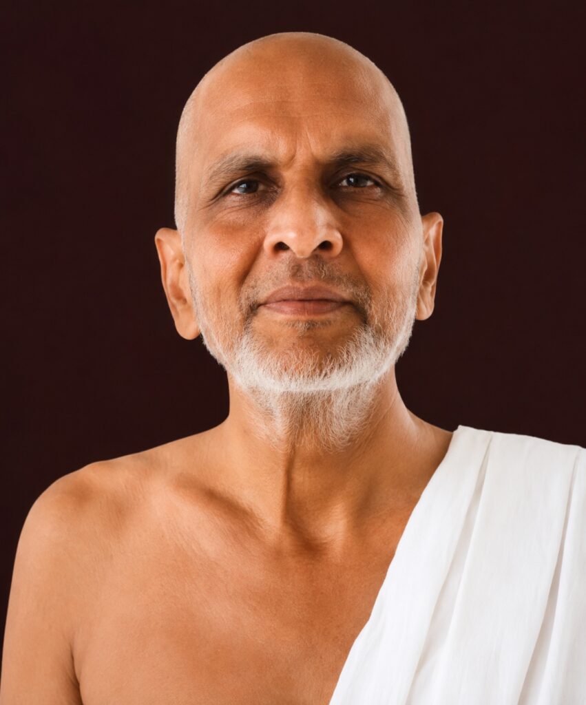 Portrait of a bald, bearded older man in a white draped robe against a dark background, facing the camera.