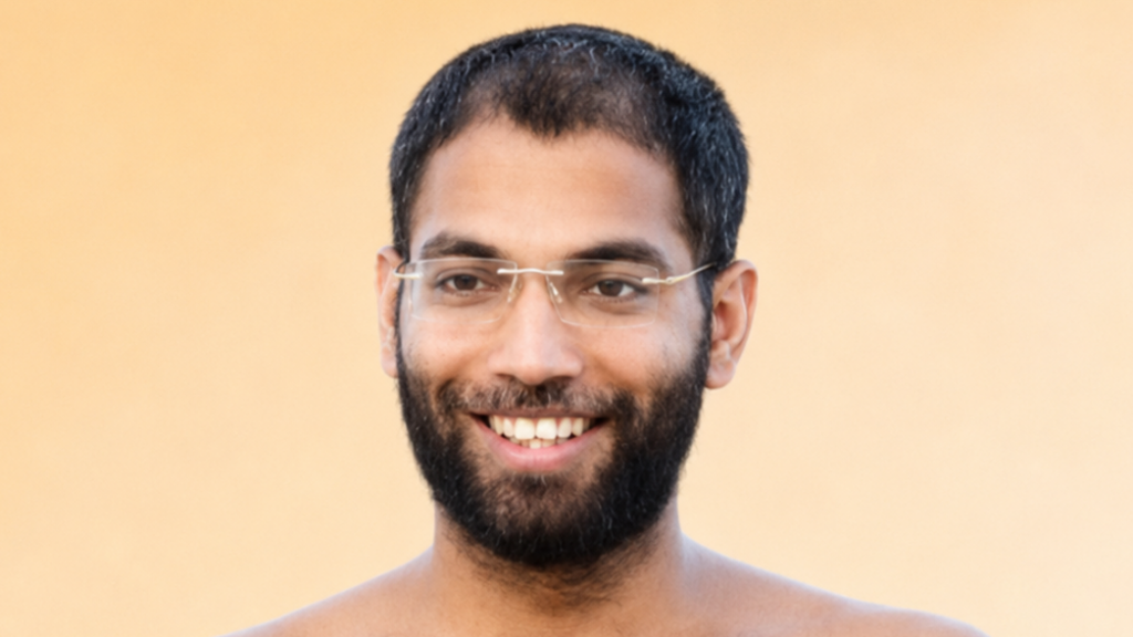 Portrait of a smiling man with a beard and glasses against a peach background, bare shoulders visible.