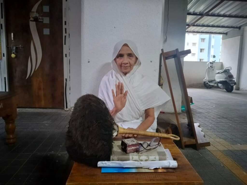 Life-size cutout of an elderly woman in a white hijab and robe, raising her right hand, set on a table in an outdoor area.