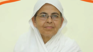 Portrait of an elderly woman wearing a white headscarf and glasses, looking at the camera.