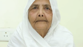 Close-up portrait of an elderly woman wearing a white headscarf, looking at the camera.
