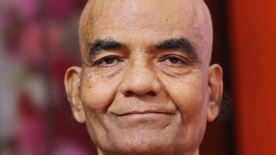 Close-up of a smiling bald man with a calm expression against a reddish background.