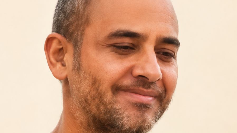 Close-up of a smiling man with short dark hair and light stubble, looking downward.