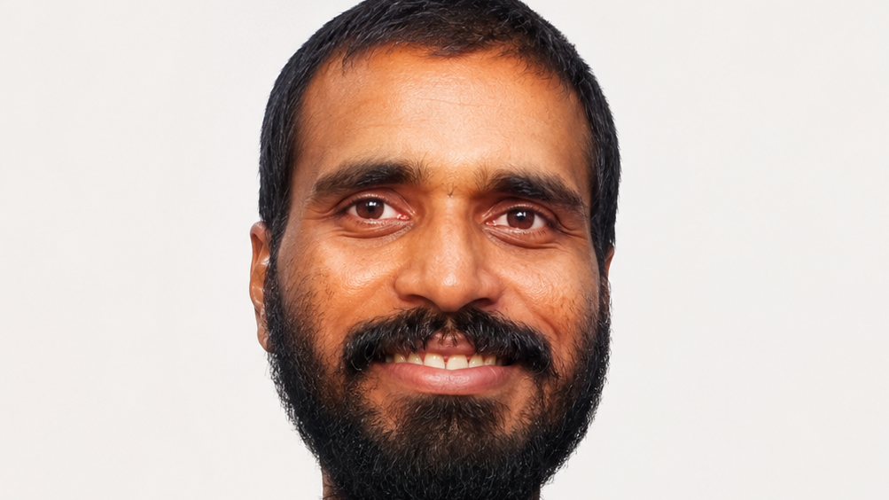 Close-up portrait of a smiling man with a dark beard against a light background.