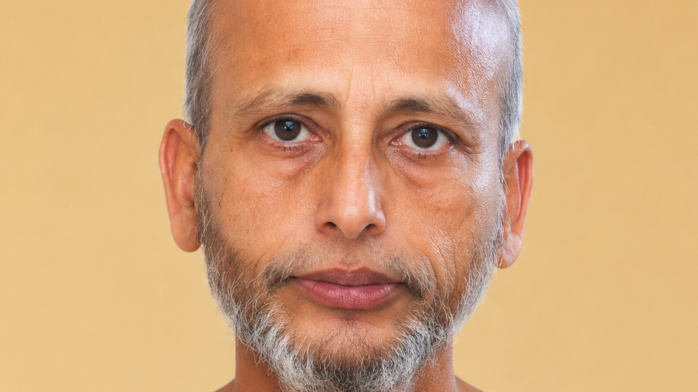 Close-up portrait of a middle-aged man with a gray beard, looking straight at the camera against a warm yellow background.