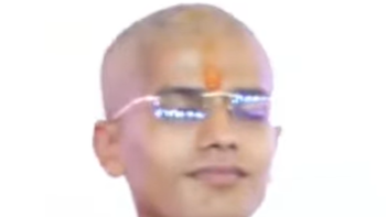 Portrait of a man with a red tilak on his forehead, wearing glasses, against a white background.