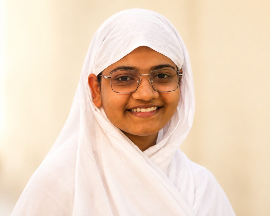Portrait of a smiling girl wearing a white hijab and glasses, facing the camera.