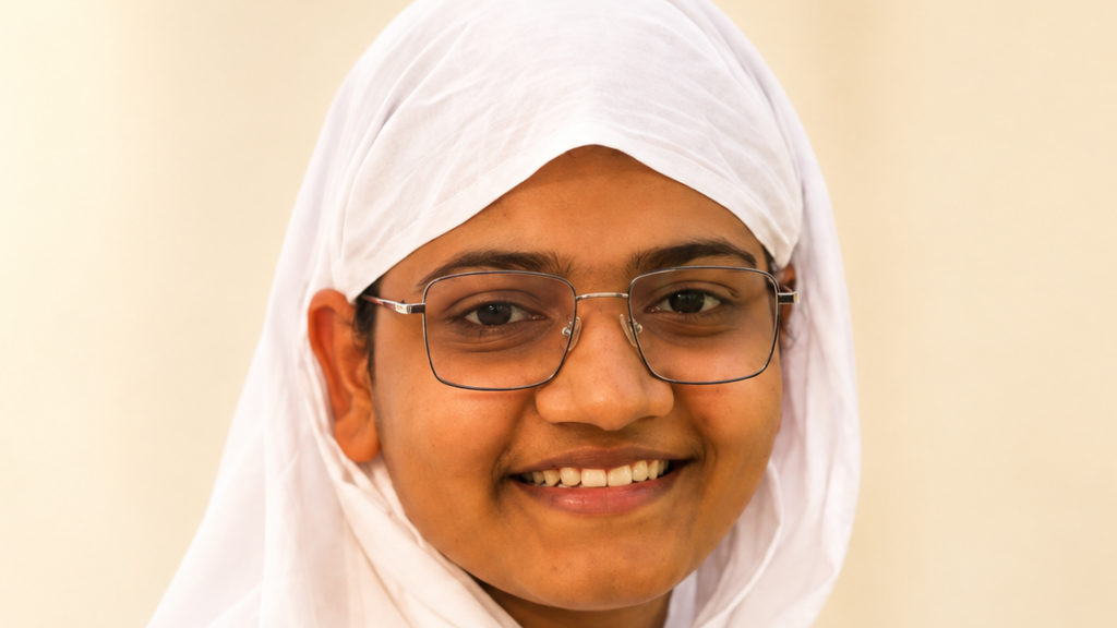 Close-up portrait of a person wearing a white hijab and metal-framed glasses, smiling warmly at the camera.