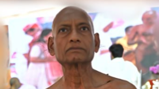 Close-up of a bald man with bare shoulders at a colorful indoor event, looking upward with a serious expression.