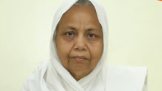 Portrait of an elderly woman wearing a white headscarf, looking at the camera with a neutral expression.