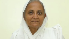 Portrait of an elderly woman wearing a white headscarf and white clothing, looking at the camera.