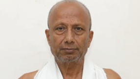 Portrait of an older man with a short gray beard, wearing a white towel over his shoulders against a white background.