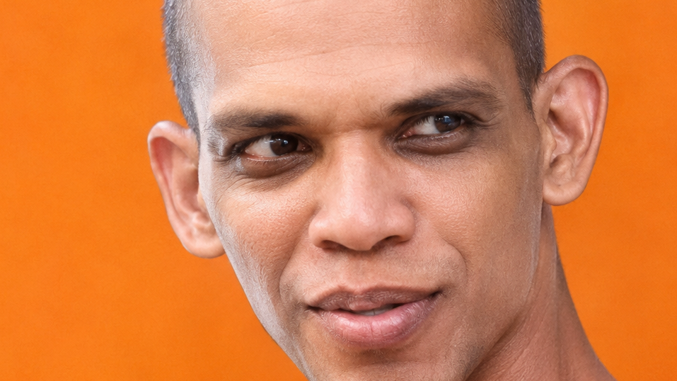 Close-up portrait of a man with an orange background, looking to the side.