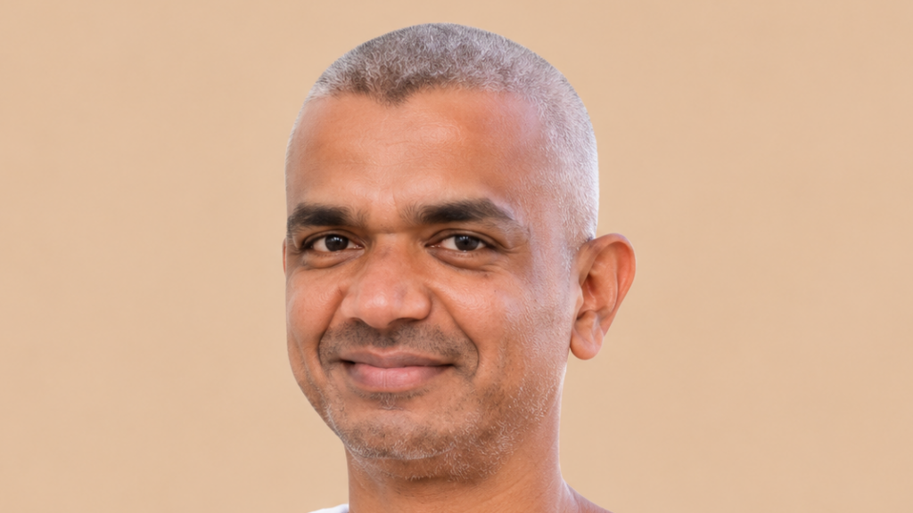 Head-and-shoulders portrait of a smiling man with short gray hair against a beige background.