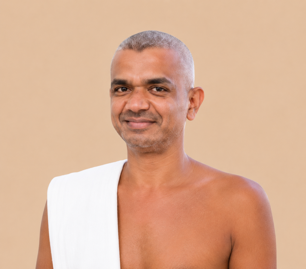 Portrait of a smiling man with short gray hair, draped in a white garment over one shoulder, against a beige background.