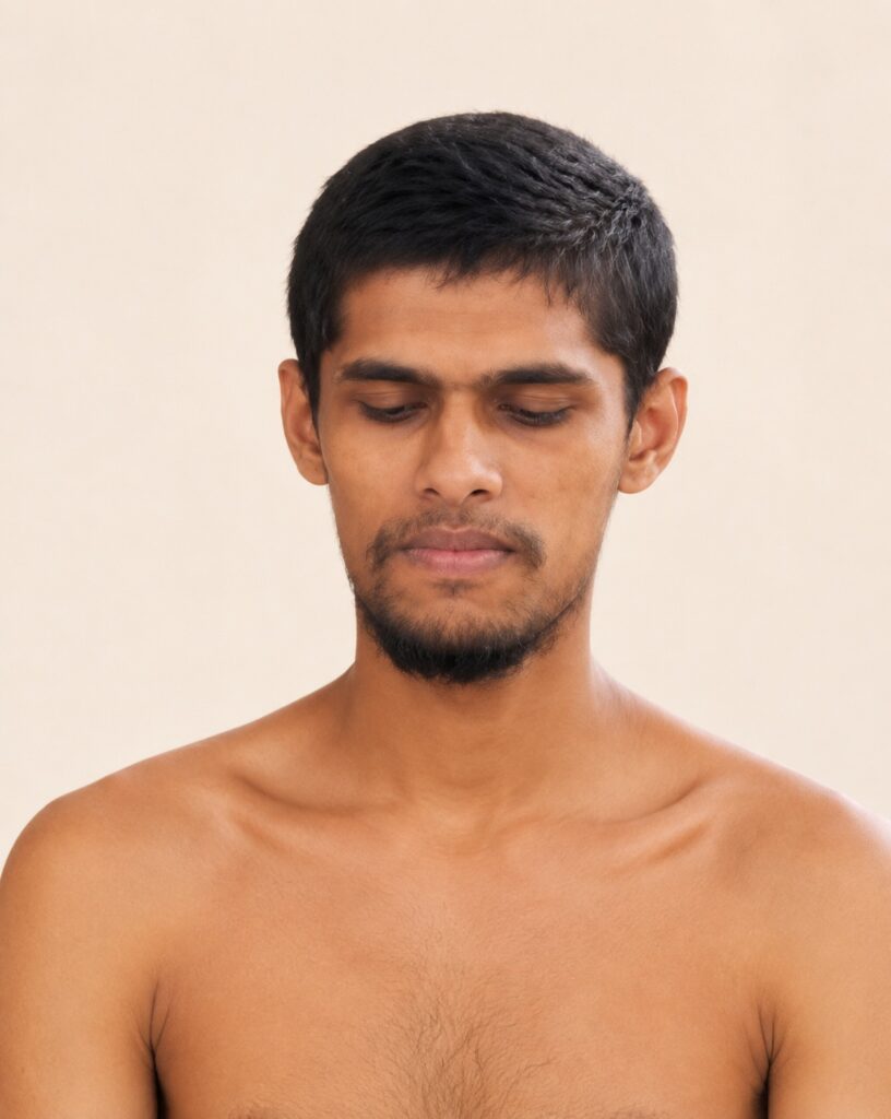 Man with short black hair and stubble, eyes closed, bare shoulders against a beige background.