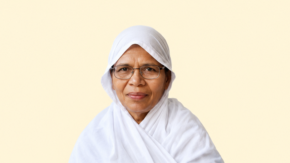 Older woman wearing a white hijab and glasses, looking at the camera against a pale yellow background.
