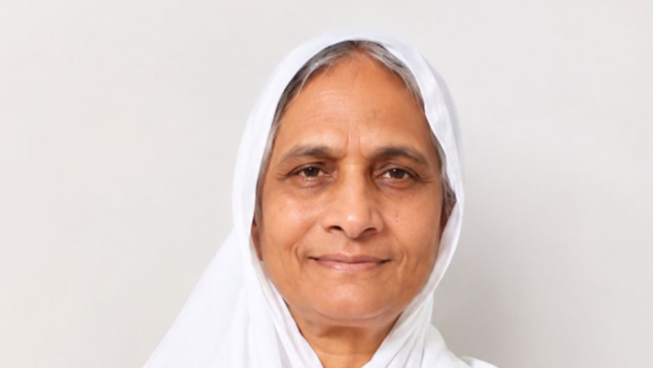 Older woman wearing a white headscarf, smiling at the camera against a neutral light background.