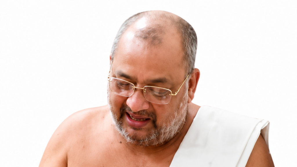 Man with glasses and a gray beard looking down, wearing a white robe against a white background.