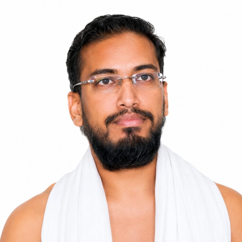 Portrait of a man with a beard and glasses, wearing a white draped cloth, looking at the camera.