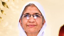 Portrait of an older woman wearing a white headscarf and glasses, facing the camera with a soft smile against a light yellow background.