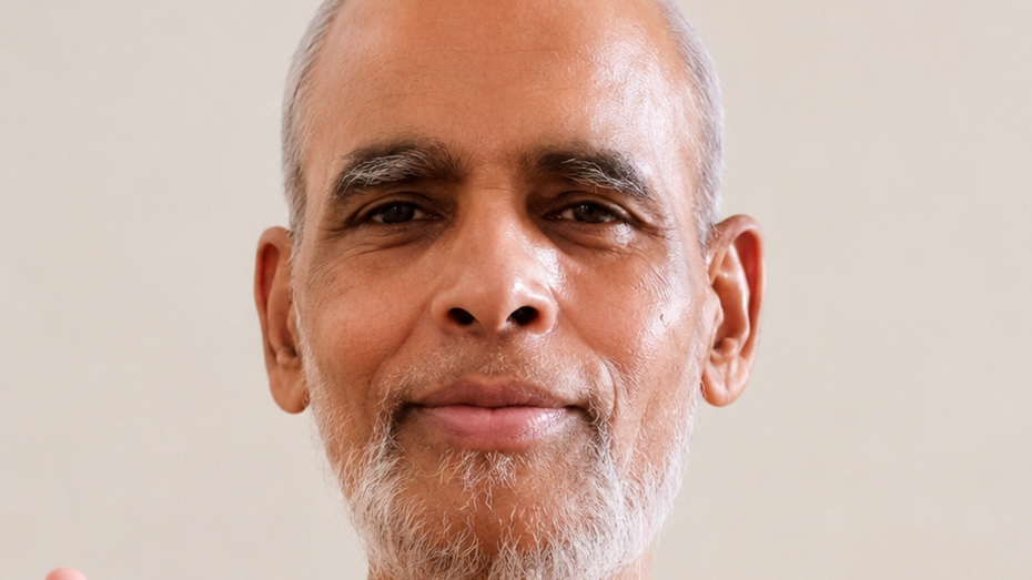 Close-up portrait of a smiling older man with a gray beard and short hair against a neutral background.