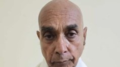 Close-up portrait of a bald man with a neutral expression against a light background.