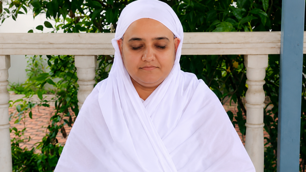 Woman in a white hijab meditating outdoors with eyes closed beside a railing and greenery.