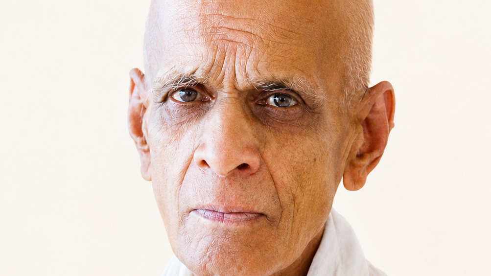 Close-up portrait of an elderly bald man with a serious expression, light skin, and a white collared shirt, looking directly at the camera.