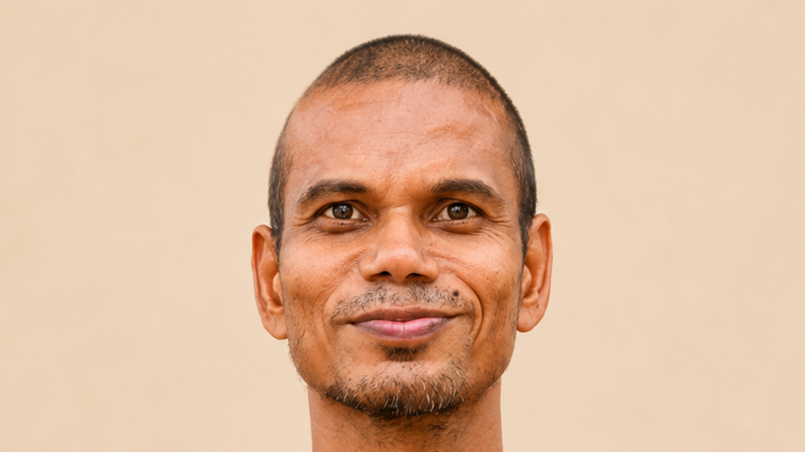 Close-up portrait of a smiling man with short hair against a light beige background.