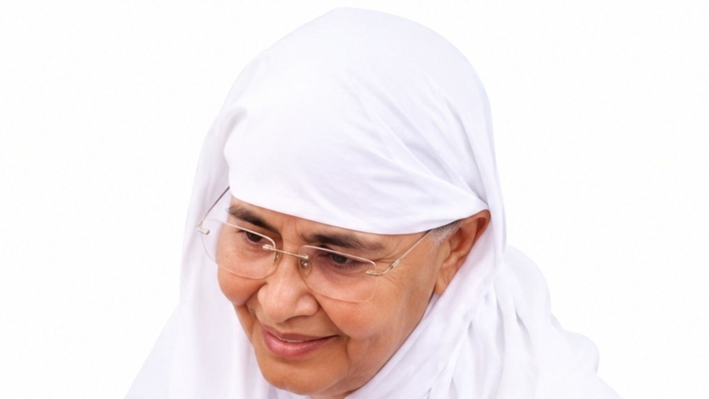 Older woman wearing a white hijab and glasses, smiling softly toward the left side of the frame