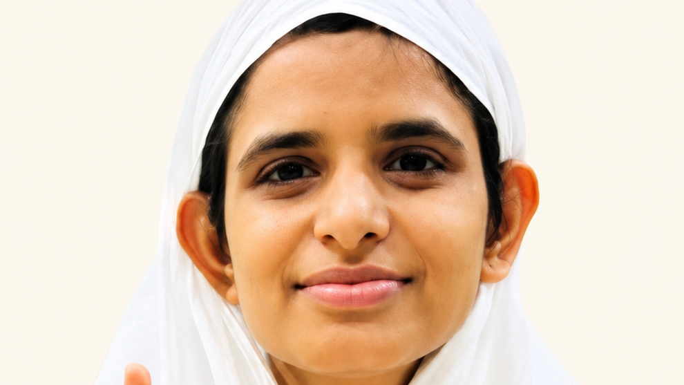 Close-up of a smiling child wearing a white headscarf against a light background.