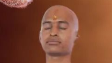 Person with shaved head meditating, eyes closed, and a yellow tilak on the forehead.