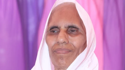 Portrait of an elderly woman wearing a white headscarf against a purple background.