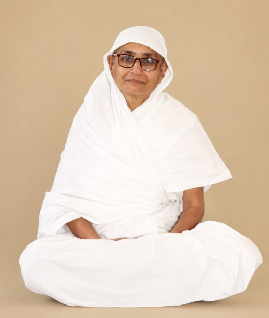 Portrait of a person wearing white traditional garments and glasses, seated cross-legged against a beige background, smiling softly.