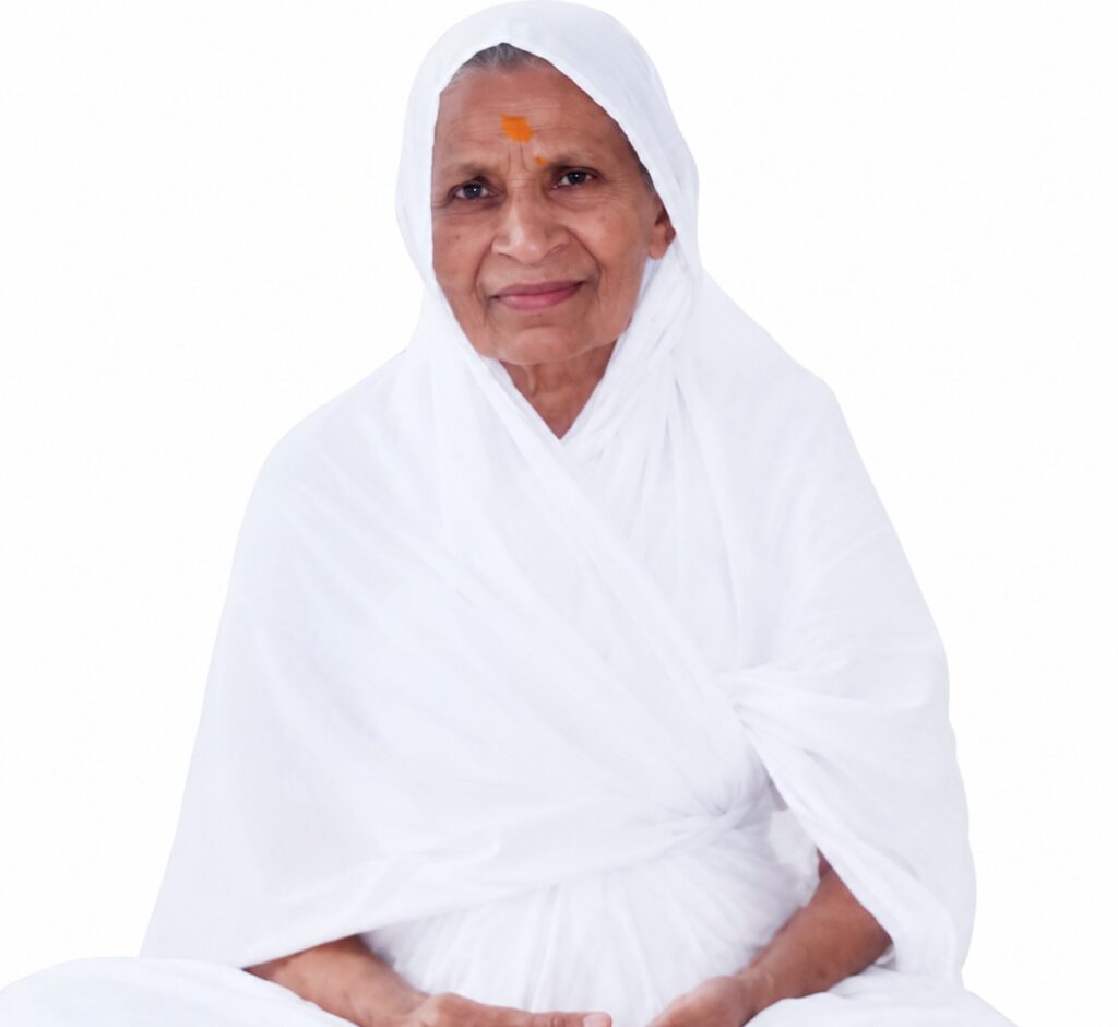 Elderly woman in white traditional attire seated and smiling, with an orange tilak on her forehead.