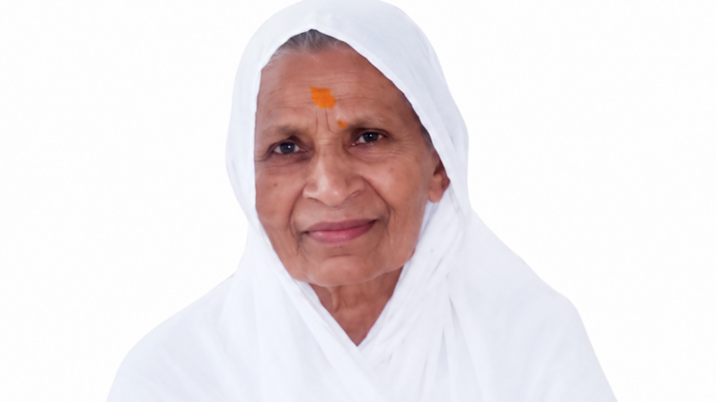 Elderly woman wearing a white headscarf, with an orange forehead tilak, smiling softly.