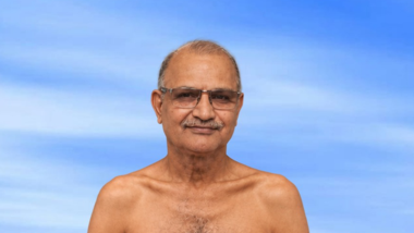 Older man with glasses and mustache, shirtless, facing the camera against a blue sky background.